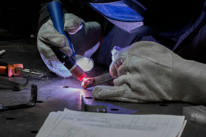 Close-up of a welder performing TIG welding on metal with protective gloves and helmet.