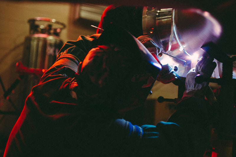 Welder performing TIG weld on stainless steel pipe with precise technique in controlled environment.