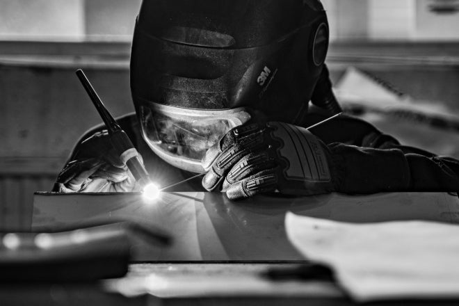 Welder using TIG process on stainless steel with helmet and gloves.