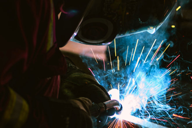 Welder in action with bright arc light and smoke, showcasing the intensity of MIG/TIG welding.